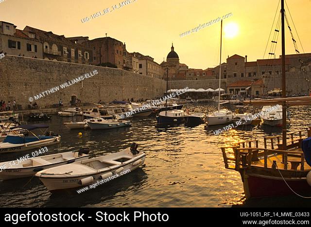 Photo of Dubrovnik City Walls at sunset and Dubrovnik Old Town Harbor, Croatia. This is a photo of Dubrovnik City Walls and the spire of the Cathedral of the...