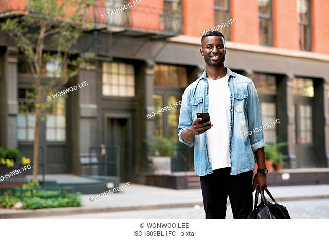 Young man with hand luggage holding cellphone in streets of New York, US