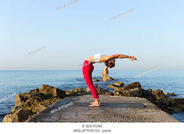 Young woman practicing yoga on the beach, doing a backdrop