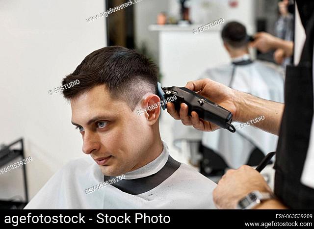 Barber trim hair with clipper on handsome man in barber shop