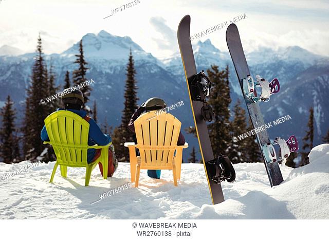 Couple sitting on chair by snowboards at snow covered mountain