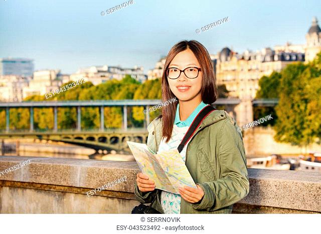 Female young tourist walking along embankment of the Seine River with map of Paris
