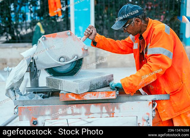 Moscow, Russia - August 14, 2015: a builder cuts a piece of granite stone on a circular saw machine. Reconstruction of pavement tiles in the capital near palace...