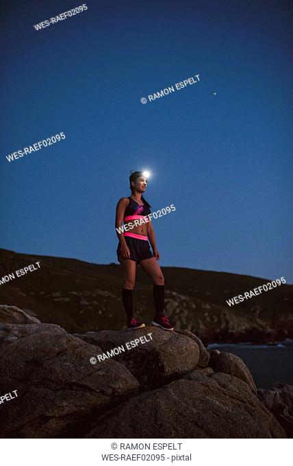 Sportive woman with headlamp standing on rocks in the evening