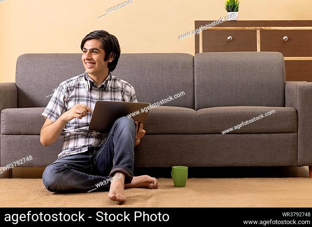 Teenage boy using laptop while sitting on floor in living room