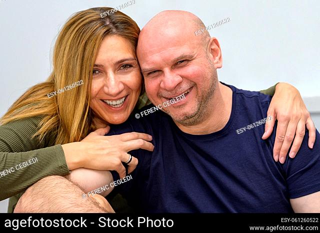 Happy loving middle aged couple with arms around each other enjoying precious time together and smiling, looking and laughing straight into the camera
