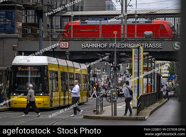 01 August 2022, Berlin: A streetcar stands at a stop at Friedrichstraße station while a regional train passes in the background