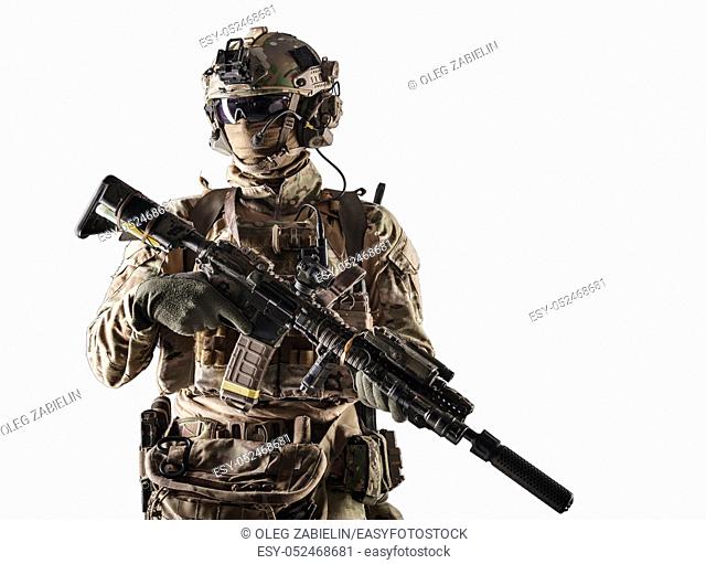 Special forces fighter in battle uniform and helmet with radio headset, face mask and ballistic glasses, standing with equipped laser sight and silencer service...