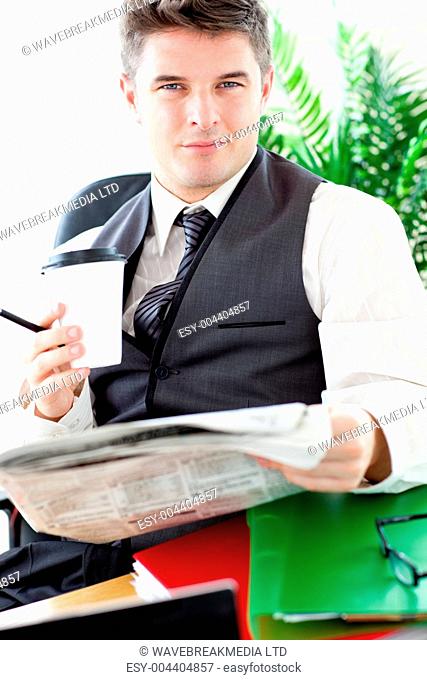 Serious businessman drinking a coffee while reading a newspaper