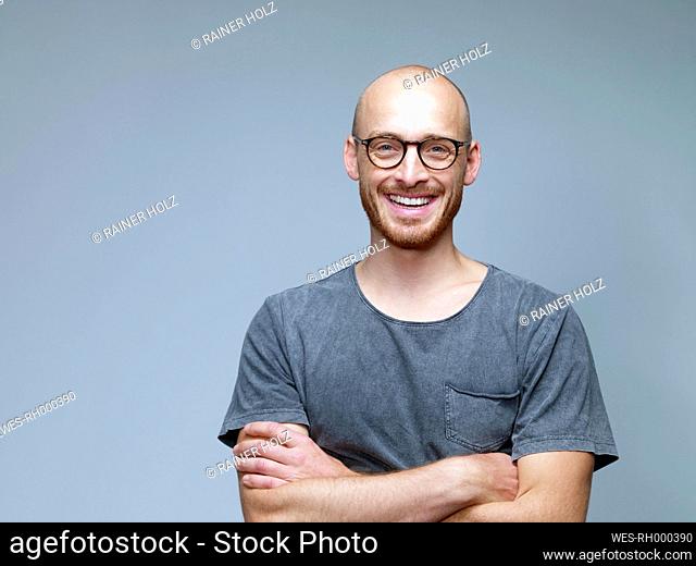 Portrait of smiling man with crossed arms in front of grey background