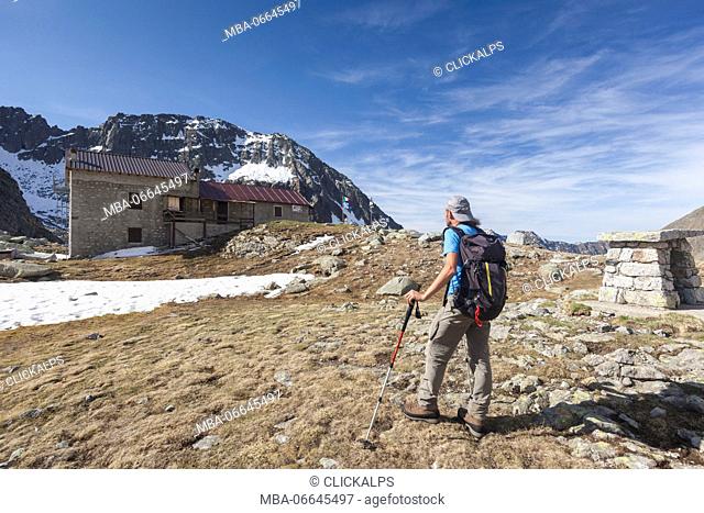 Hiker towards Rifugio Tonolini framed by high peaks Val Malga Adamello Regional Park province of Brescia Lombardy Italy Europe