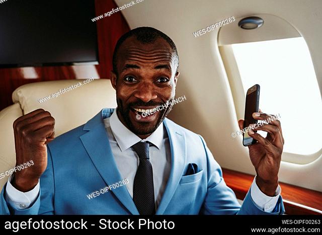 Happy male entrepreneur with smart phone in private jet