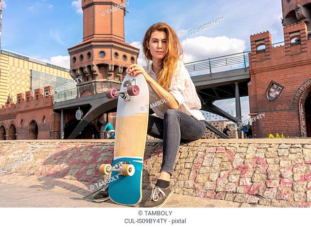Young woman with skateboard resting on Oberbaum bridge in city, Berlin, Germany