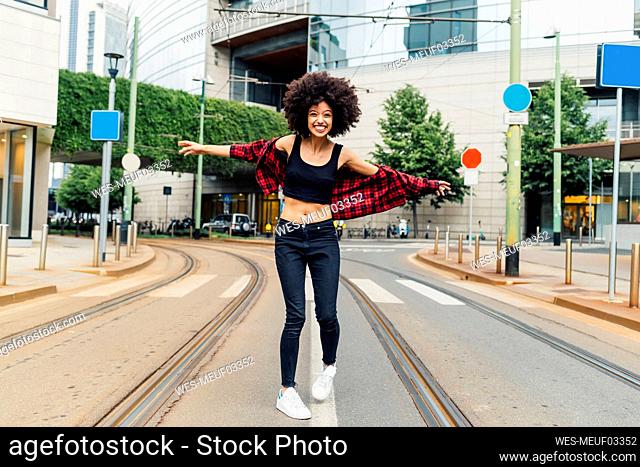 Happy woman with arms outstretched standing on tramway in city