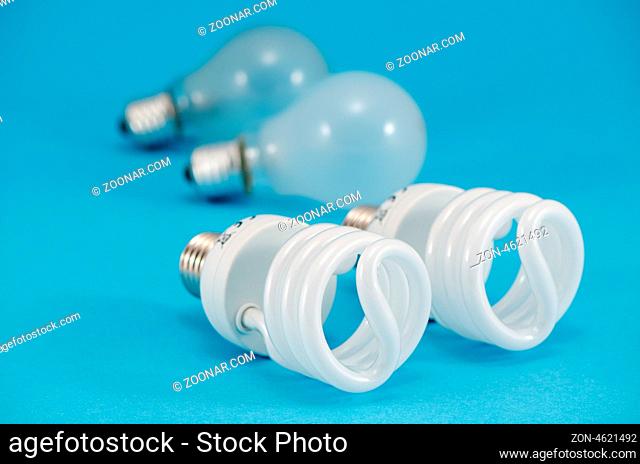 two pair of new and old bulbs. novel modern fluorescent lights and old incandescent heat bulb on blue background. economic technology for less electricity...