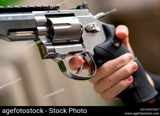 in one hand is large silver heavy revolver and aims into the air