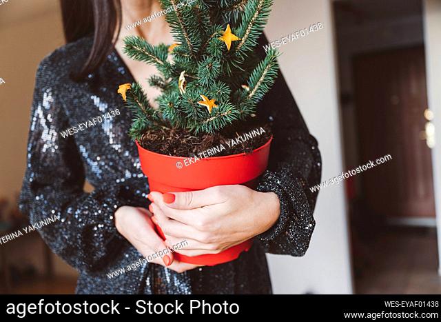 Woman wearing glittering dress holding Christmas tree while standing at home