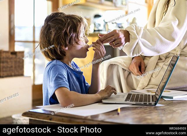 young boy at home having his temperature taken with a thermometer