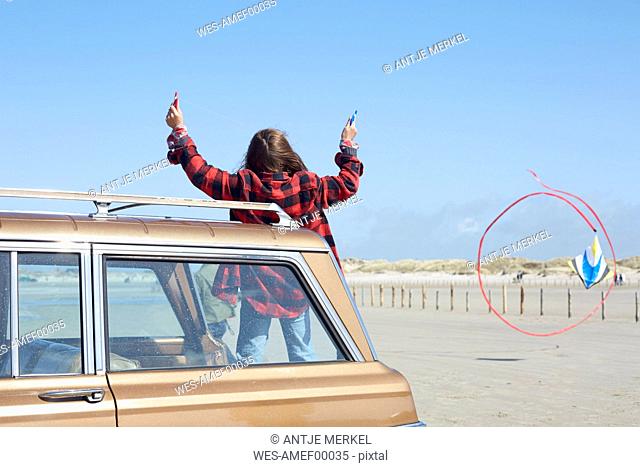 Germany, St Peter-Ording, girl flying kite on the beach from a car
