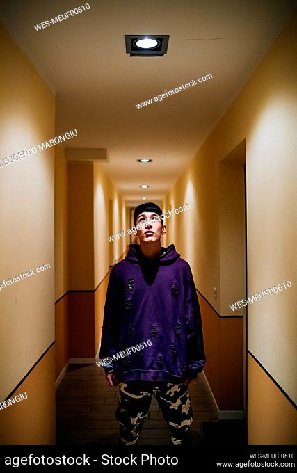 Young man looking at illuminated lighting equipment on ceiling in corridor