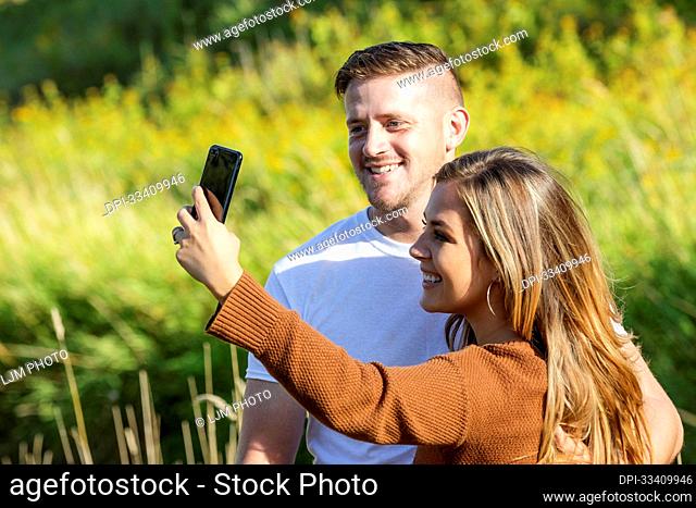 Husband and wife spending quality time together outdoors and taking a self-portrait in a city park; Edmonton, Alberta, Canada