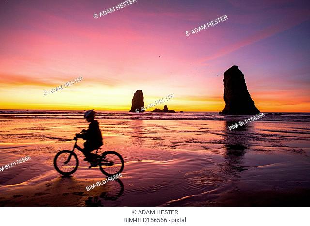 Silhouette of Caucasian girl biking near rock formations on Cannon Beach, Oregon, United States