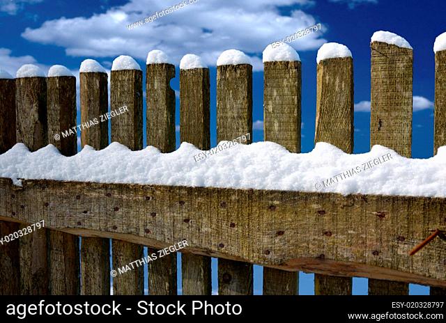 Schneebedeckter Holzzaun vor blauem Wolkenhimmel