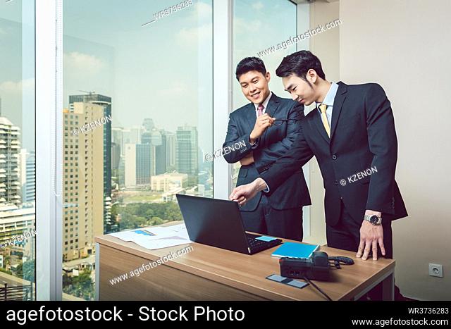 Happy young businessman showing on laptop to his colleague