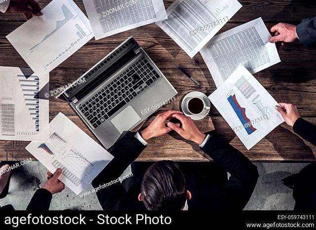 Paperwork and deadline concept - stressed businessman with papers and charts sitting at table in office