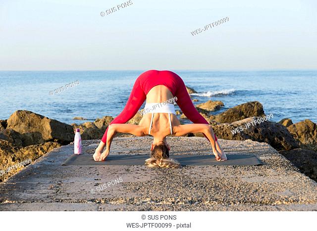 Young woman practicing yoga on the beach, doing prasarita padottanasana