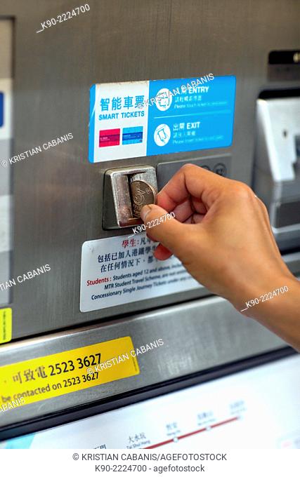Woman putting a five Dollar coin into the slot of a ticket vending machine at a MTR station, Central, Hong Kong, China, East Asia