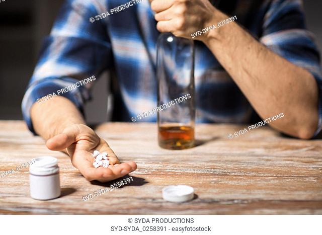 unhappy drunk man with bottle of alcohol and pills