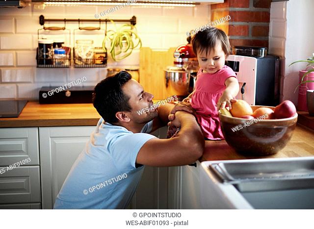 Smiling father looking at baby girl sitting on counter in kitchen at home