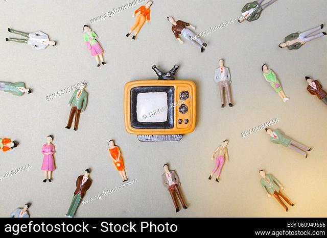 Figurine people around retro syled tiny television on yellow background