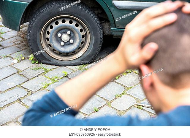 Close-up Of A Worried Man With Hand On Head Looking At Punctured Car Tire