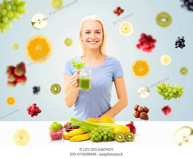 healthy eating, vegetarian food, diet, detox and people concept - smiling woman drinking green vegetable juice or shake from glass over fruits and berries on...