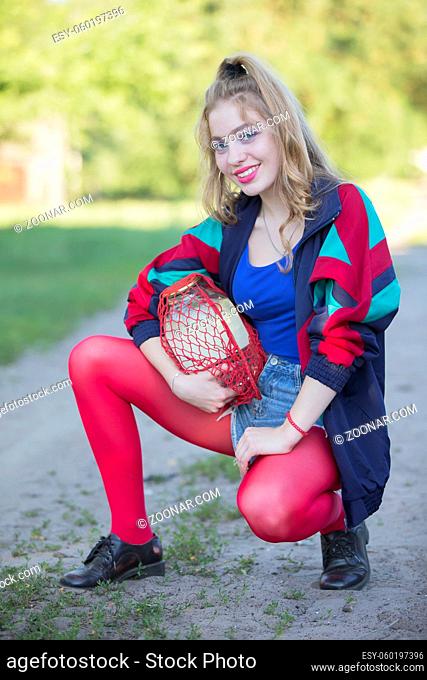 A beautiful 90s country girl in bright clothes holds a string bag with a can of birch sap. Russian Woman in the style of the 90s
