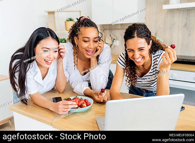 Happy friends eating fruits doing video call on laptop at home