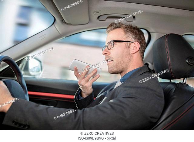 Businessman driving car, speaking into smartphone