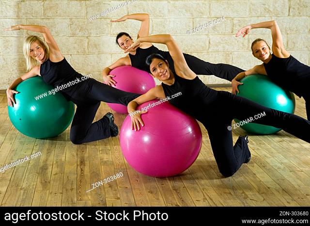 A group of women making exercise leaning on big balls. They're smiling and looking at camera. Front view