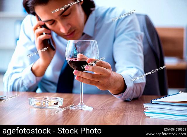 The male employee drinking alcohol and smoking cigarettes at workpla