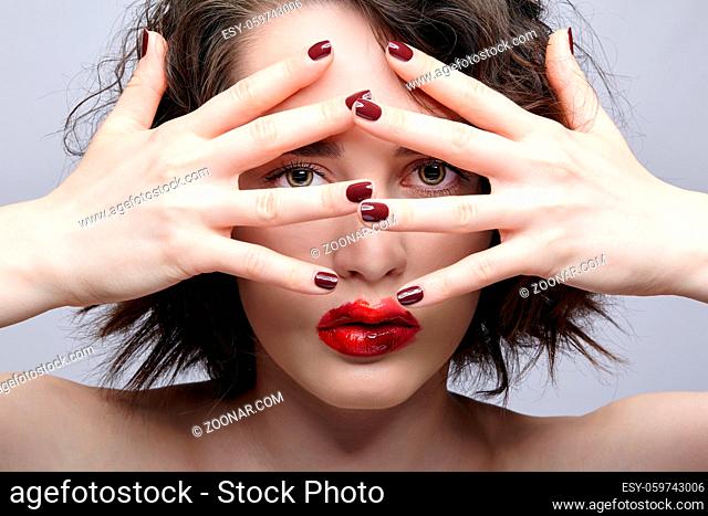 Beauty portrait of young woman with hands near face. Brunette girl with unusual alyapy red female face makeup