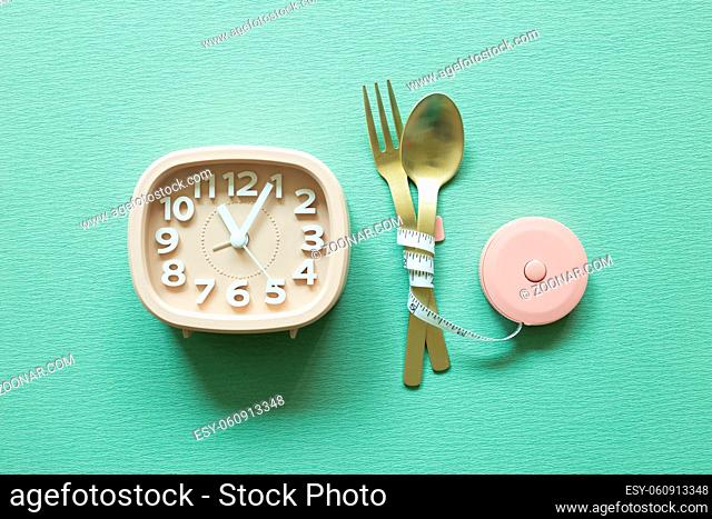 Fork and spoon with measuring tape, clock on green background. Diet concept