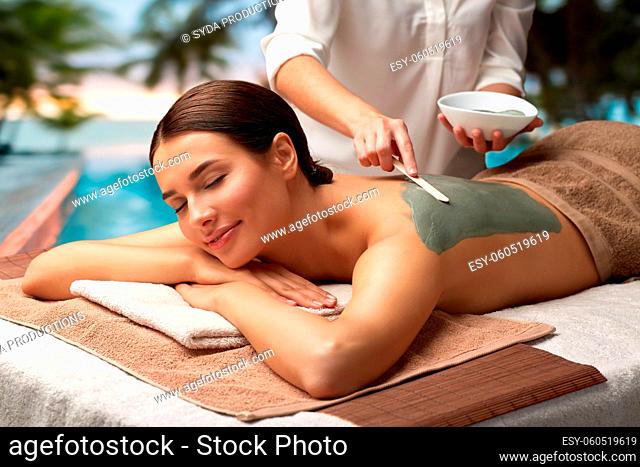 woman and cosmetologist applying clay mask in spa