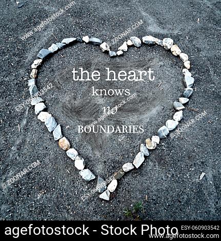 A heart made of colorful stones on sandy ground with the text the heart knows no boundaries