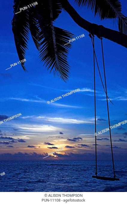 A beautiful sunset on the beach of Fihalhohi Island, the Maldives, with the palm tree and beach swing silhouetted agains the setting sun