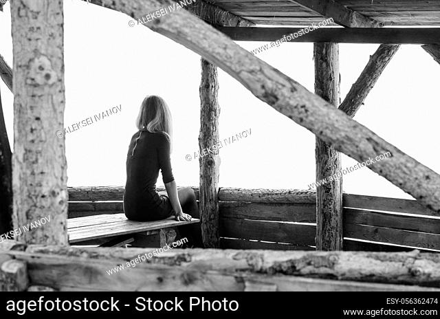 Girl alone sits early in the morning on a foggy day in a wooden arbor