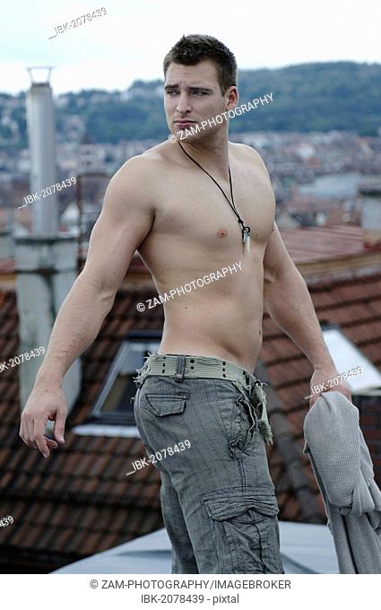 Bare-chested young man wearing jeans standing on a rooftop, Stuttgart, Baden-Wuerttemberg, Germany, Europe