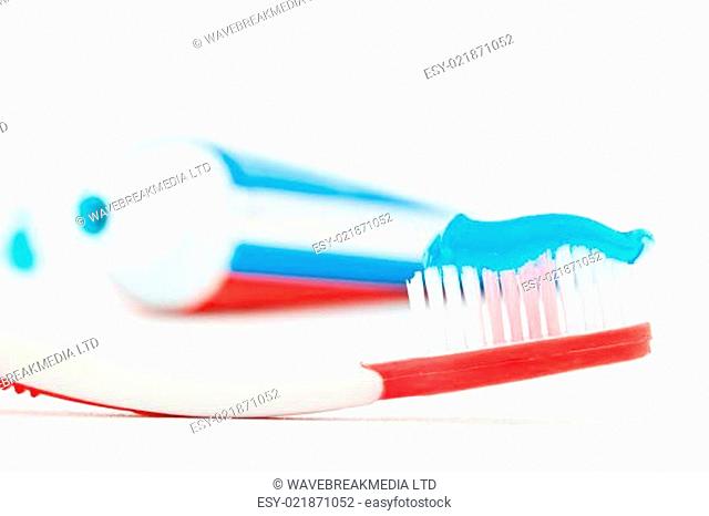 Tube of toothpaste next to a red toothbrush against white background