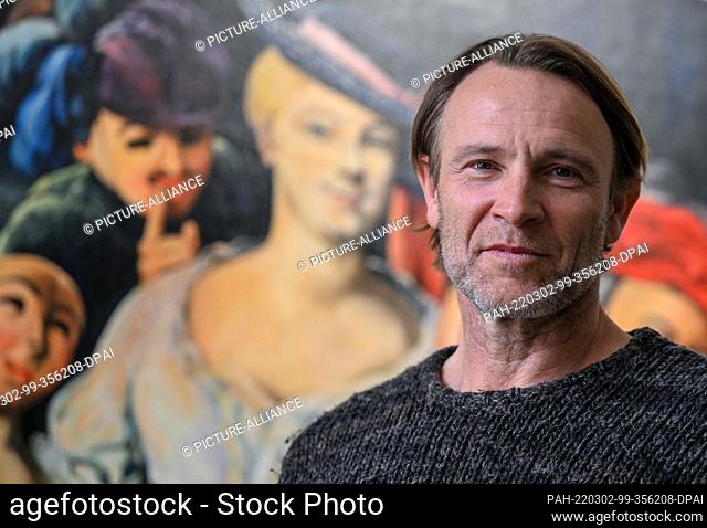 02 March 2022, Saxony, Reichenbach: Actor Bernhard Bettermann stands in front of a painting with the portrait of Friederike Caroline Neuber by artist Lidia...